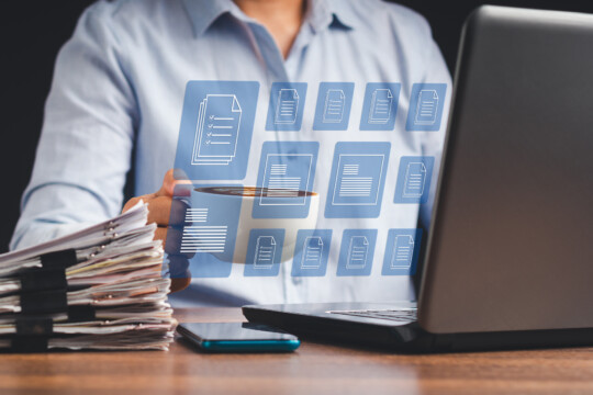 Person working at a laptop with paper files and digital document icons displayed in an interface.