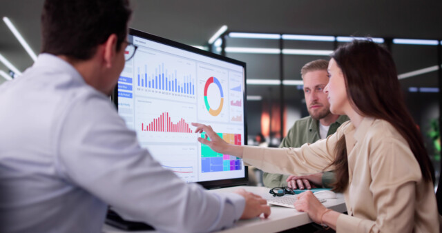 People reviewing charts and graphs on a large analytics dashboard displayed on a screen.