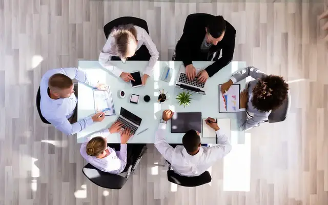 Overhead view of a diverse team collaborating around a conference table with laptops and tablets.