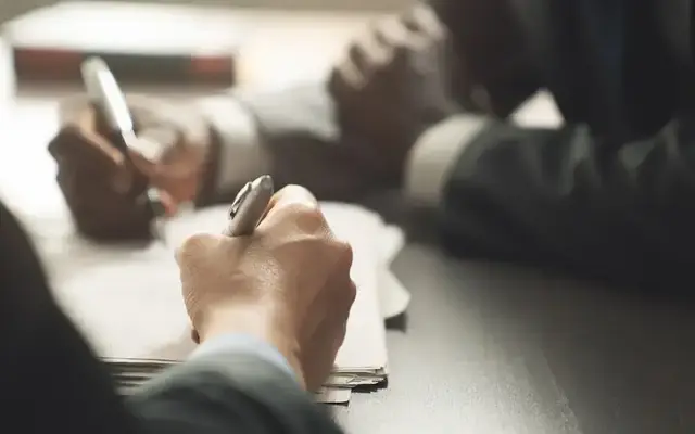 Business professionals signing documents at a table, representing a contract agreement or new business award.
