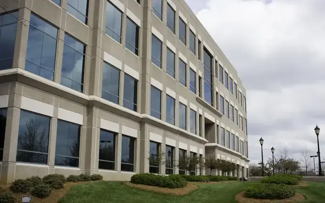 Modern multi-story office building with large windows and landscaped grounds.