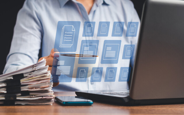 Person working at a laptop with paper files and digital document icons displayed in an interface.