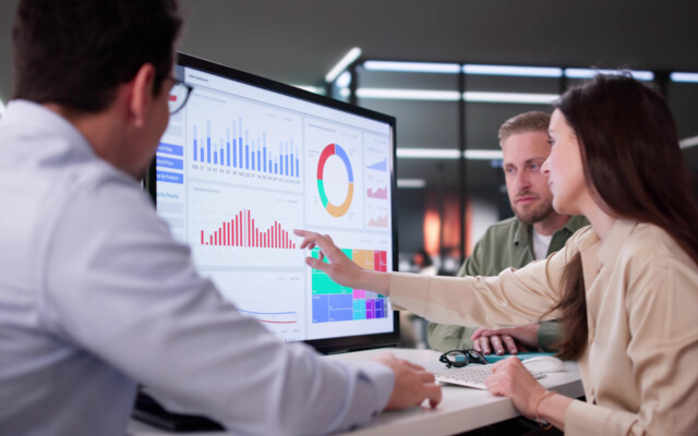 People reviewing charts and graphs on a large analytics dashboard displayed on a screen.