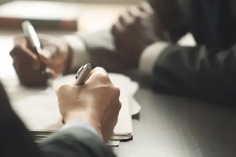 Business professionals signing documents at a table, representing a contract agreement or new business award.