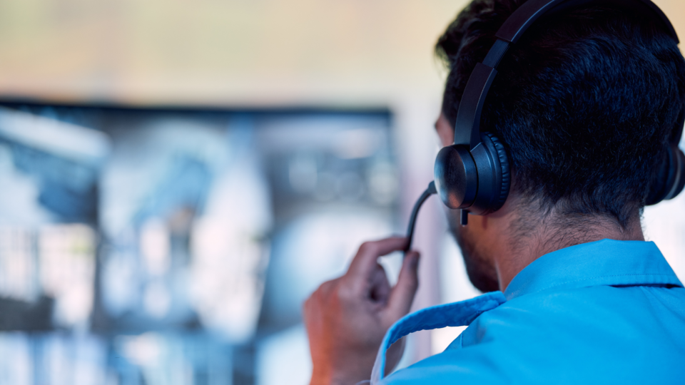 a male police dispatcher wearing a headset and looking at the dispatch board on his computer monitor