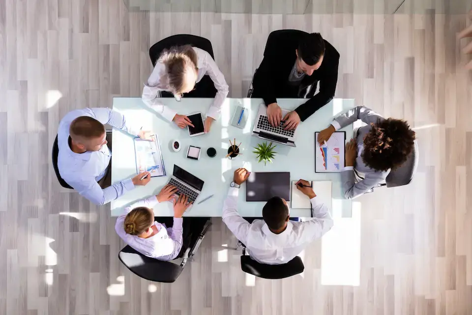 Overhead view of a diverse team collaborating around a conference table with laptops and tablets.