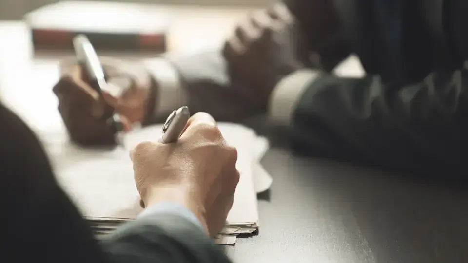 Business professionals signing documents at a table, representing a contract agreement or new business award.