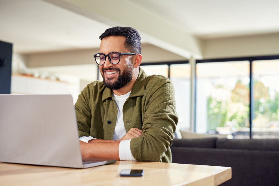 man in green shirt smiling as he works on his laptop