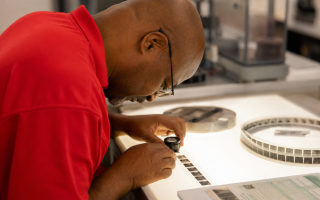 Intellinetics micrographics specialist using a loupe and light table to inspect microfilm frames for image quality and completeness.