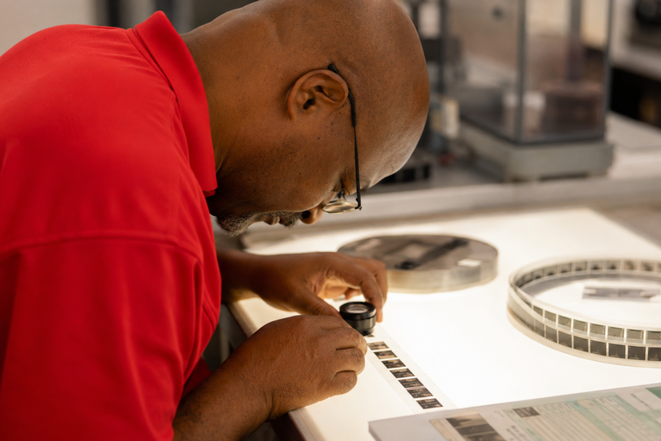 Intellinetics micrographics specialist using a loupe and light table to inspect microfilm frames for image quality and completeness.