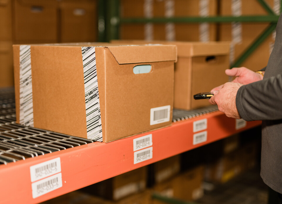 man using a handheld barcode scanner to read a barcode on a box of stored records
