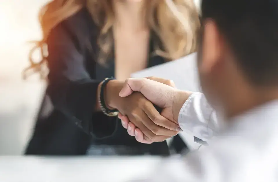 Two professionals shaking hands during a business meeting, representing a new career opportunity.